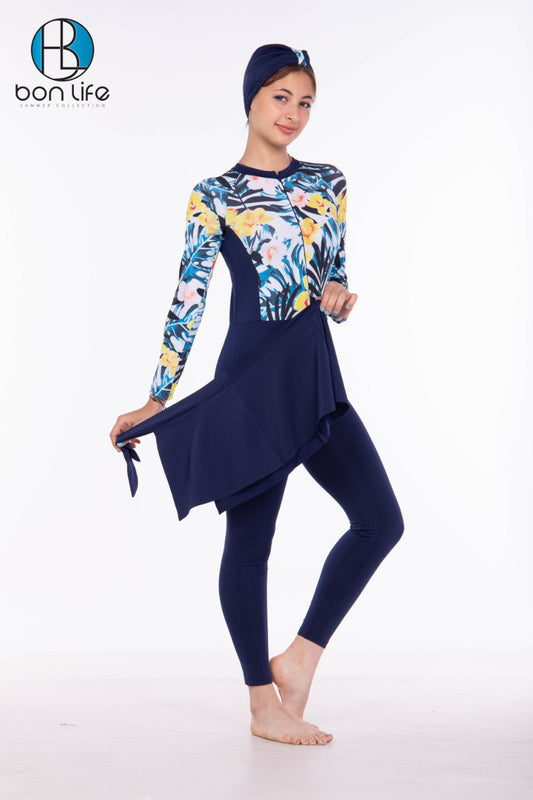 Woman wearing a floral long-sleeve top and navy blue pants with a matching headscarf, standing against a white background.
