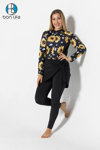 Woman wearing a black long-sleeve top with sunflower pattern and black pants on a white background, featuring the brand 'bon life'.