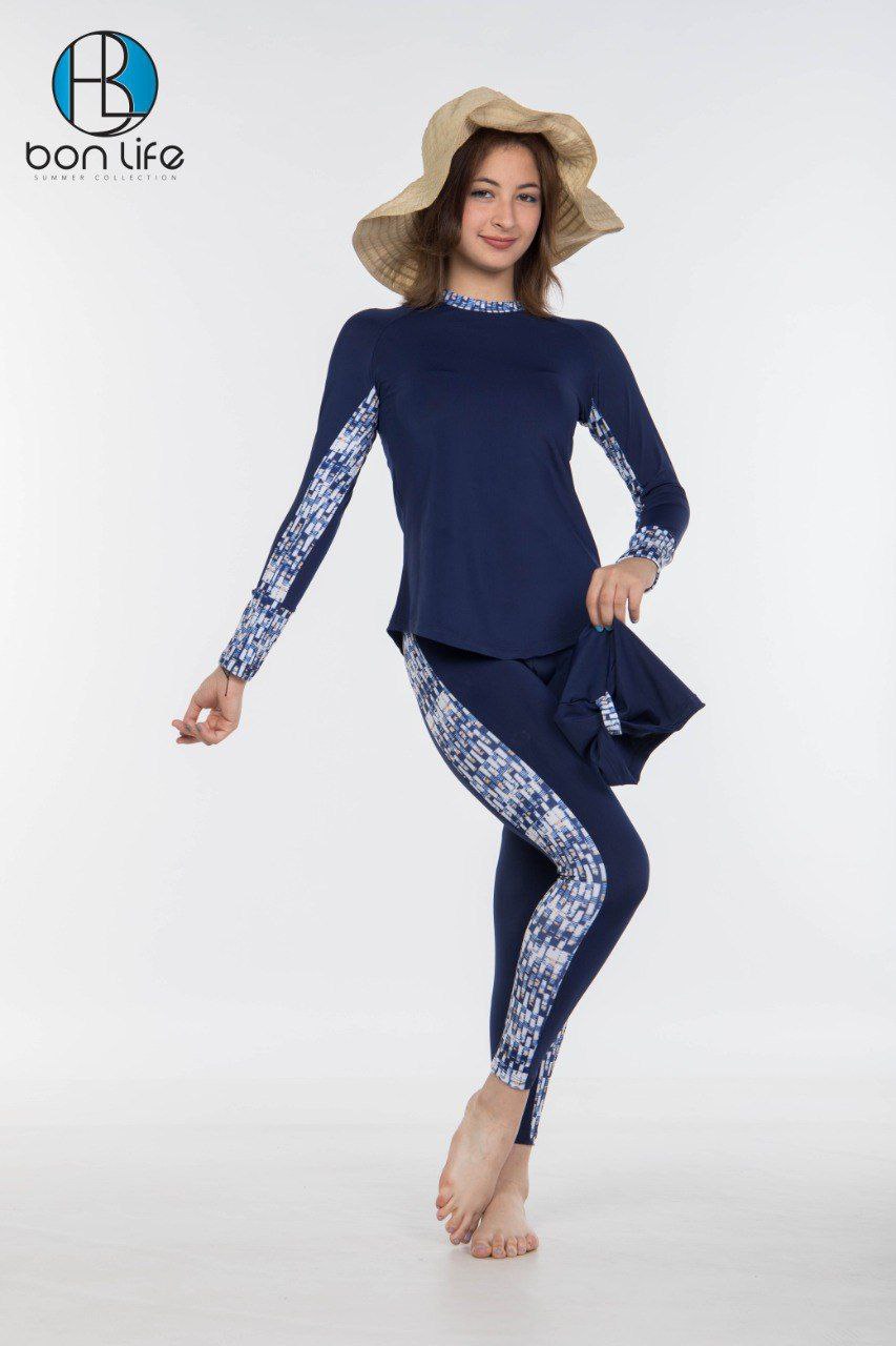 Woman wearing a navy blue swimsuit with white patterns and a matching hat on a white background.