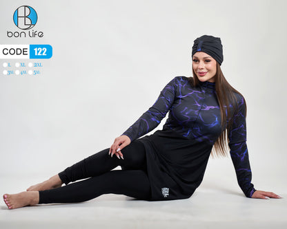 Woman wearing a black and purple outfit with a headscarf, sitting on a white background.